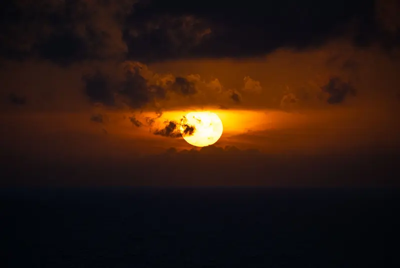 海面上的火紅夕陽，雲層壓在太陽上方