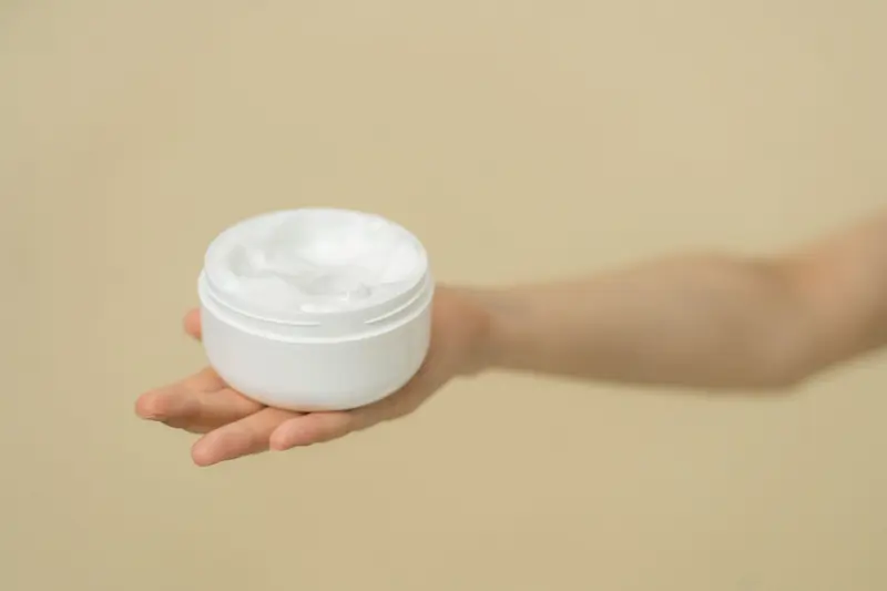 手掌托著白色乳霜罐，米色背景